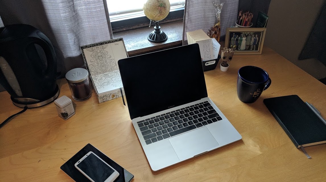 A desk with various objects including a laptop, Android devices, a notebook, and coffee mug